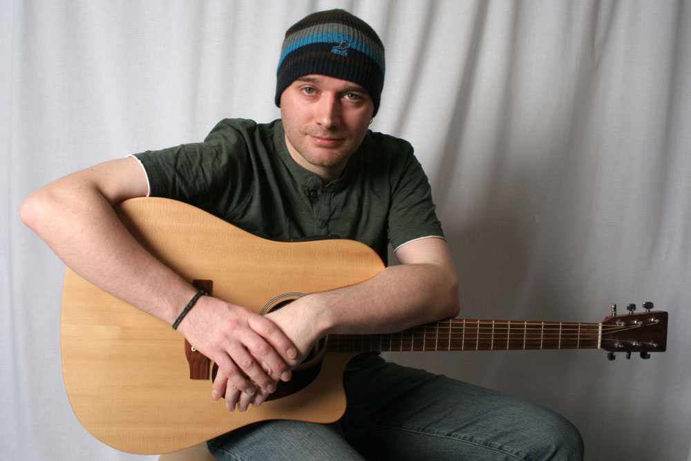 John Moxey leaning on acoustic guitar